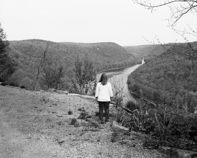 BW image of a woman's back looking out on to land and a river