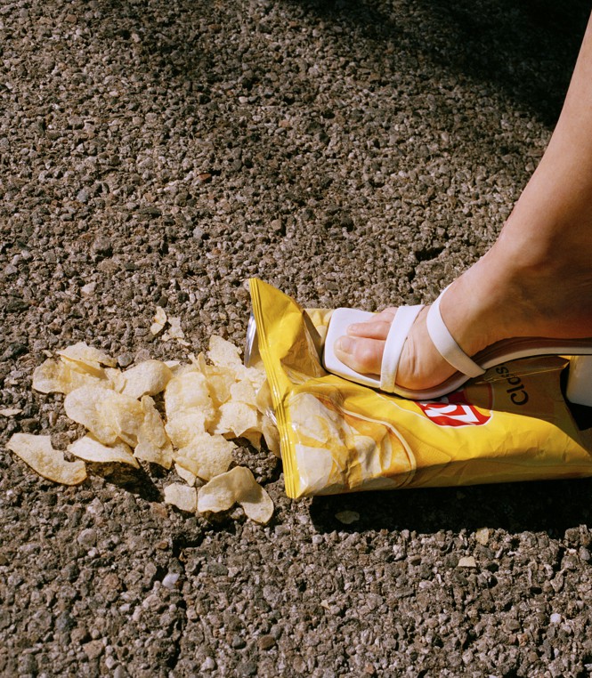 a woman's foot steps on a bag of groceries in a parking lot