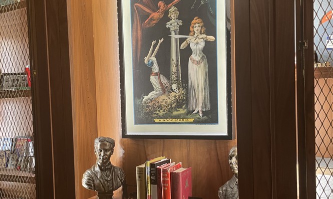 Magic memorabilia in a wooden display case, including a poster showing a woman chopping off another woman's head with a sword.