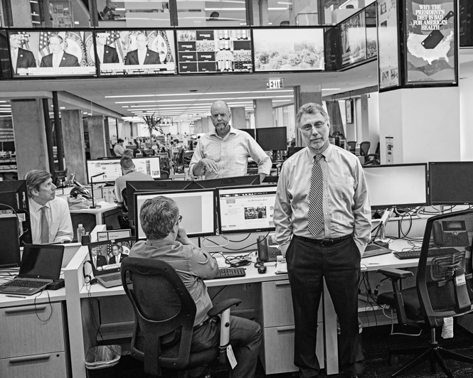 Black-and-white photo of Martin Baron standing in Washington Post newsroom near working reporters, desks, and screens