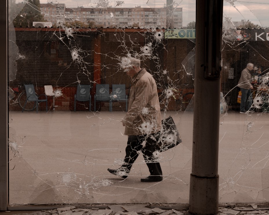 a man walks in front a a window riddled with bullet holes