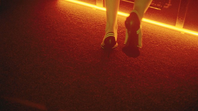 The back of a person's ankles as they walk away from the camera, wearing black heels with white stripes.