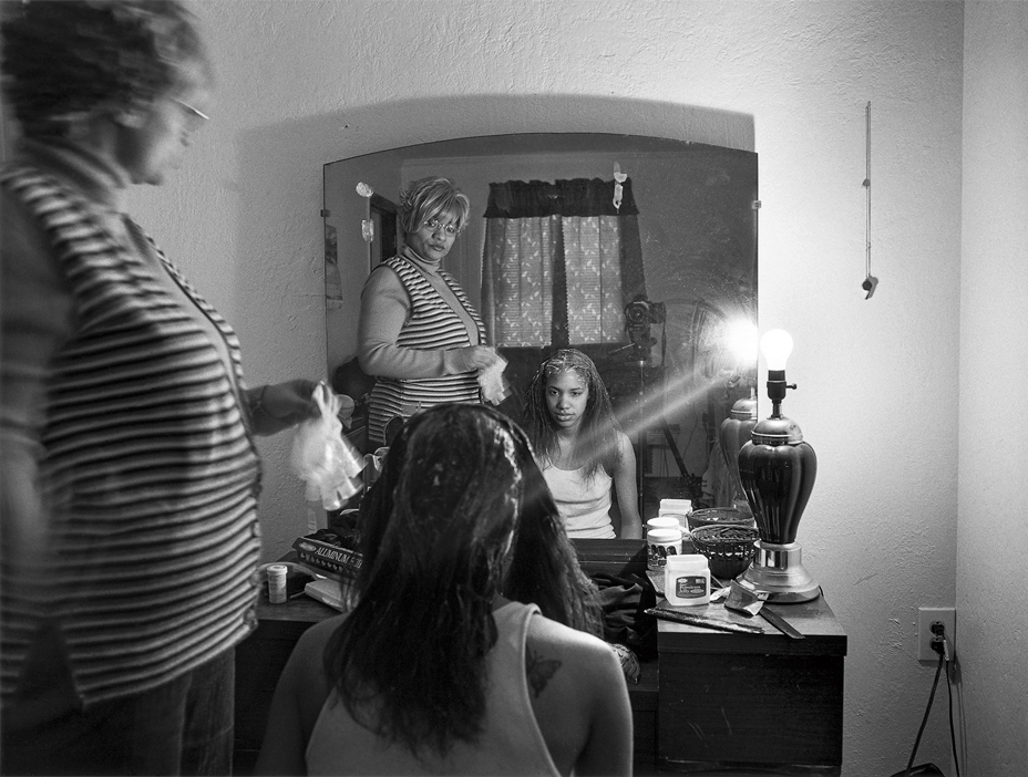 black-and-white photo of woman standing with girl seated, both looking into mirror