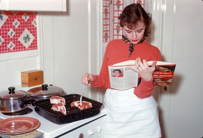 A woman reading a cookbook next to the stove