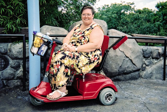 photo of woman in floral print dress and sandals on red mobility scooter