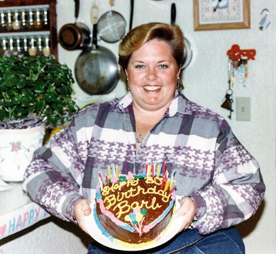 photo of woman in kitchen holding birthday cake that says 