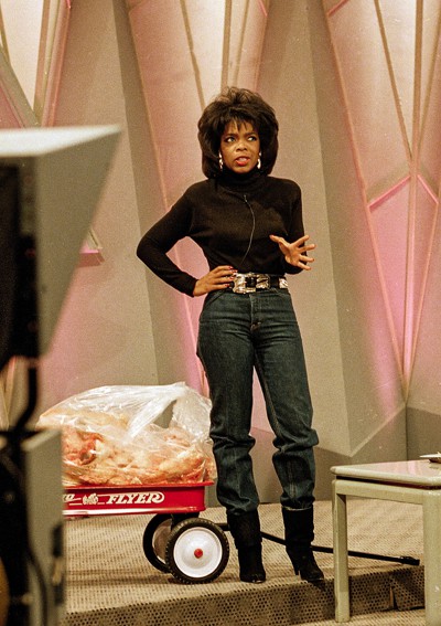 photo of Oprah Winfrey on stage talking next to red Radio Flyer wagon full of plastic bag of fat
