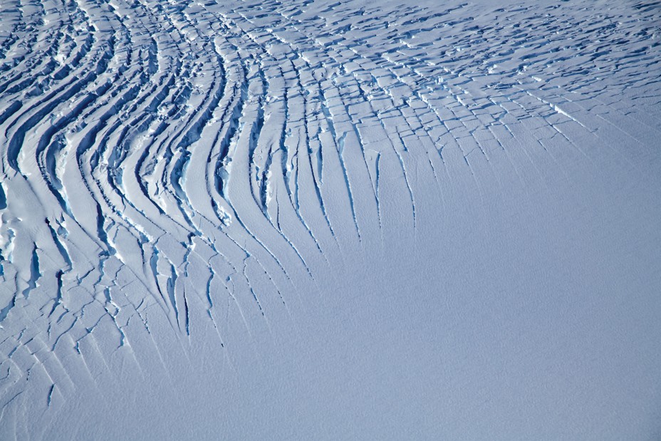 aerial photo of large snow-covered area that is smooth at bottom and toward the top breaks into curving ridges and deep gashes