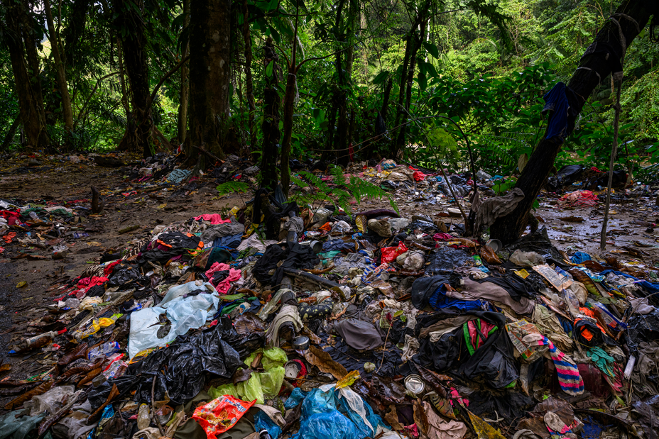 photo of piles of strewn clothing and supplies in mud with green jungle in background