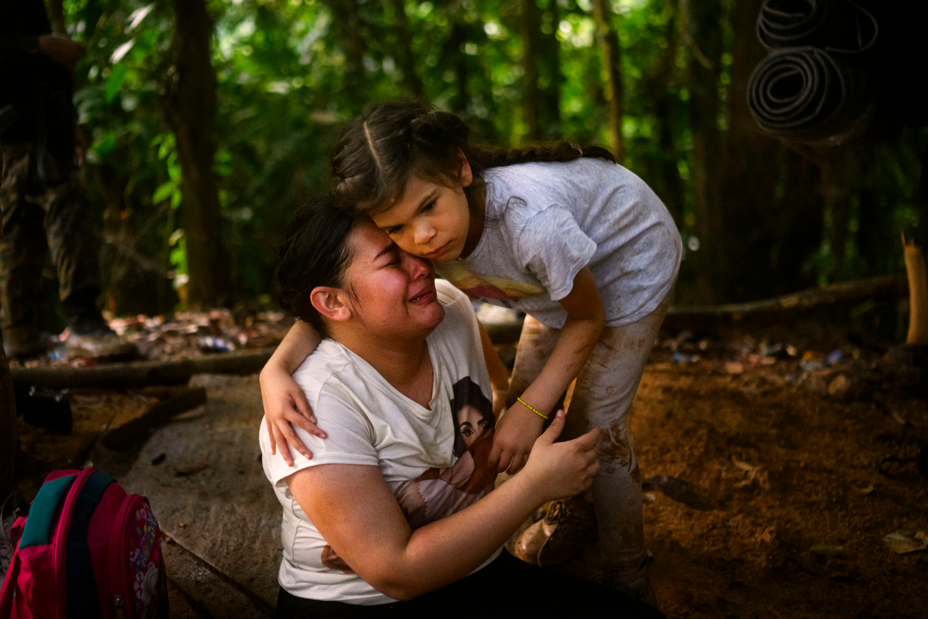photo of small girl standing and bending down to hug a crying woman seated on the ground