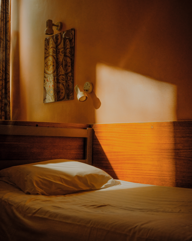 photo of twin bed with pillow in dorm room with slant of golden light streaming through window