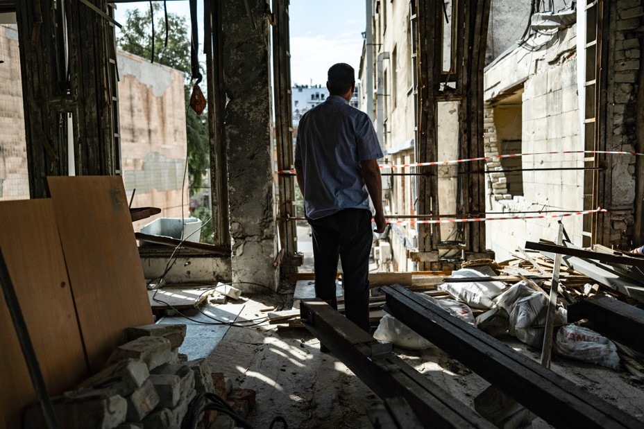 A man stands with his back to the camera looking outside in a bombed out room in Ukraine.