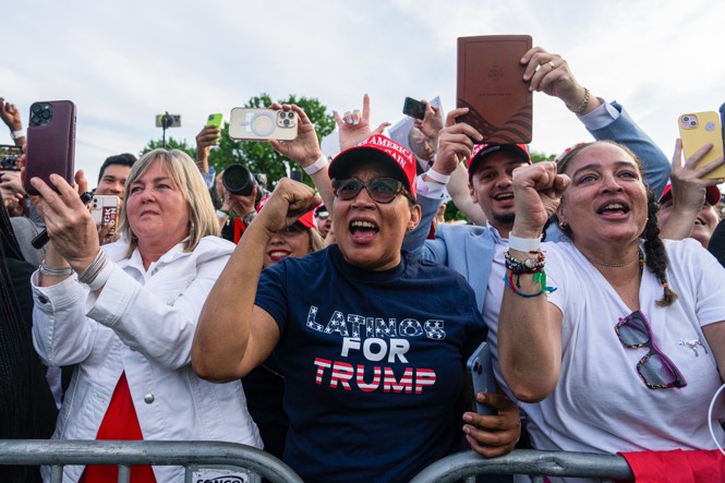 A crowd of people cheer for Donald Trump at a rally.