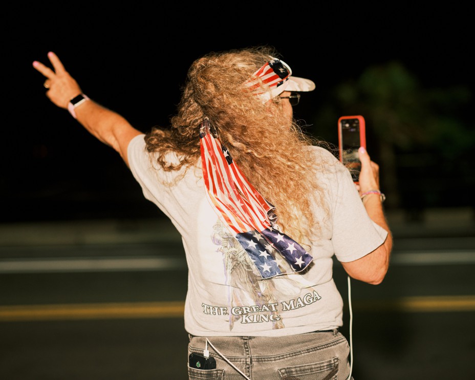 A white woman facing away from the camera throws her left arm out in the air while holding her phone