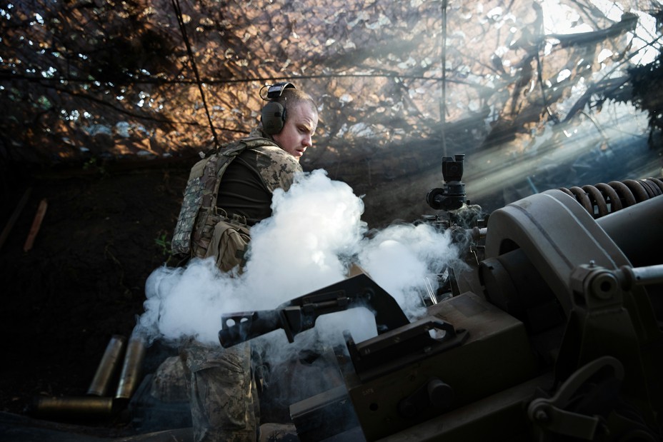 Smoke arises as a Ukrainian soldier fires a howitzer toward Russian troops.