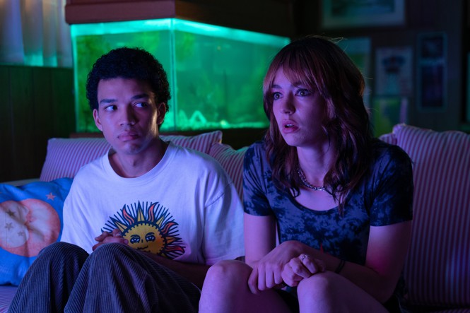 A man and a woman sit on a couch in the glow of a television