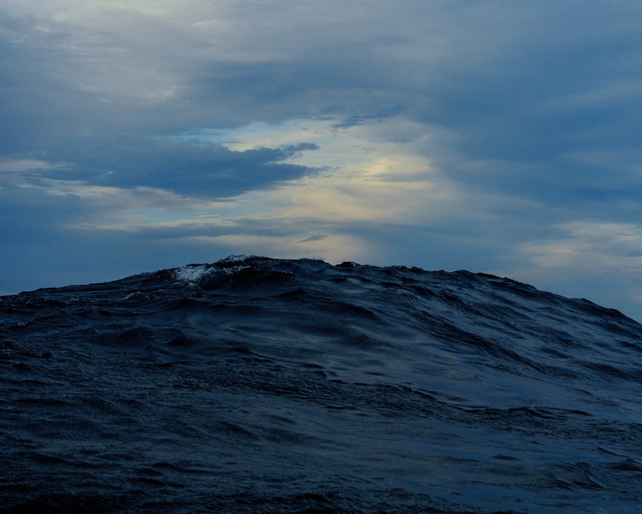 photo of large ocean wave swelling with dawn or dusk clouds in background