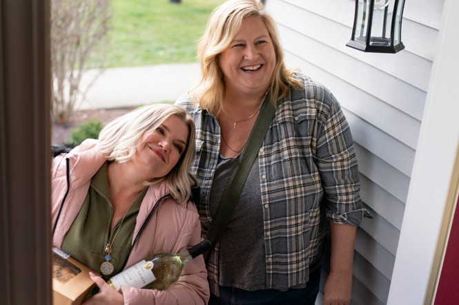 Two women stand in a doorway laughing