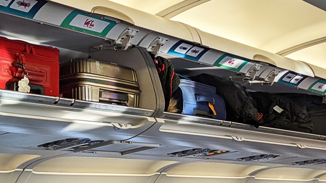 A photograph of suitcases packed into an airplane's overhead luggage bins