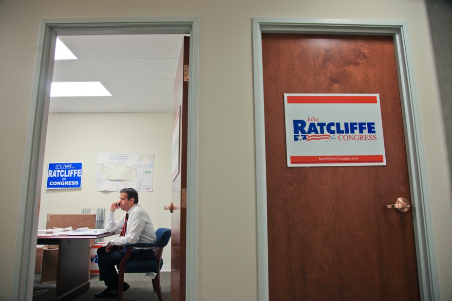 John Ratcliffe is seen in an office making a phone call through a door way with signs for his Congressional campaign