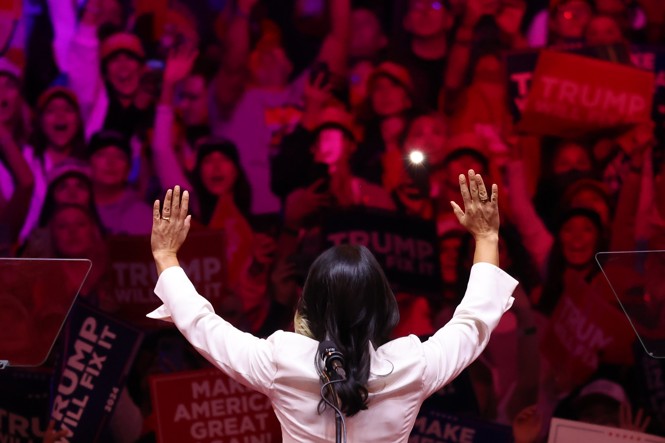 Tulsi Gabbard is seen from behind wearing a white suit waving to a crowd