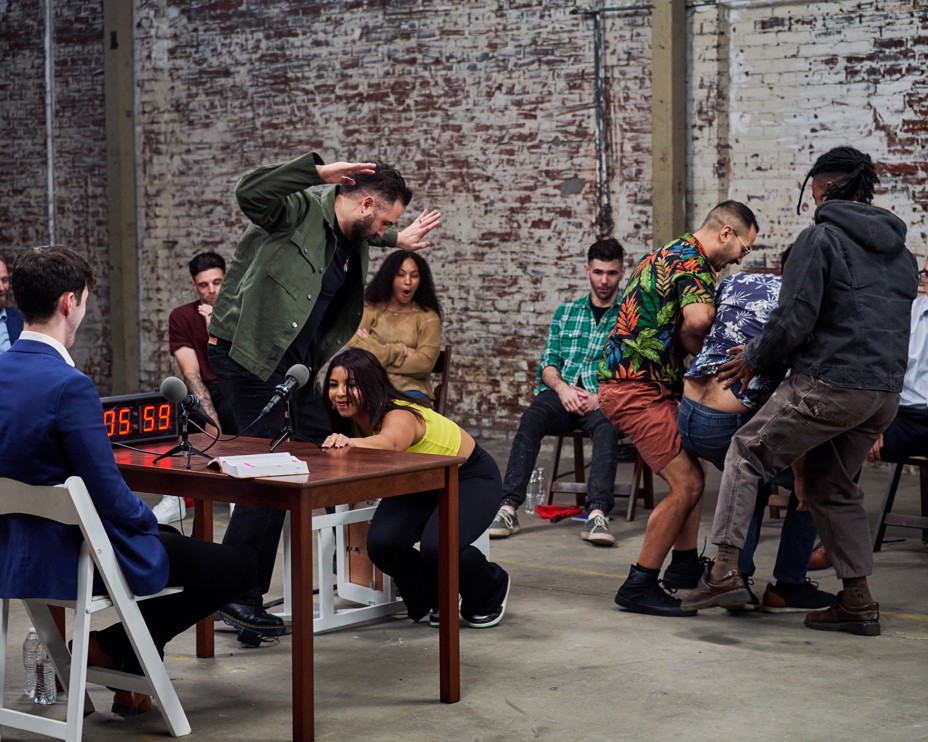 A bunch of people race to reach a table and a woman is holding onto it 