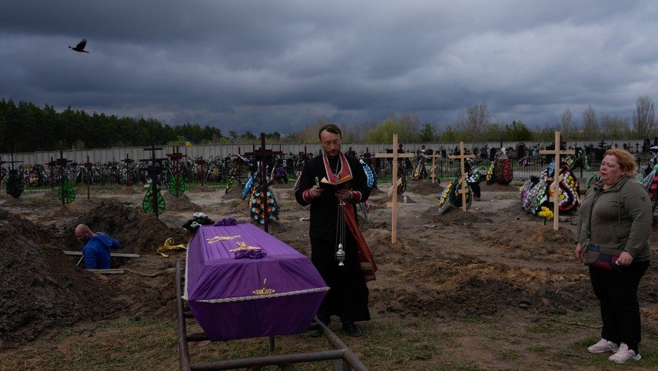 A Ukrainian priest prayers next to a casket in a cemetry