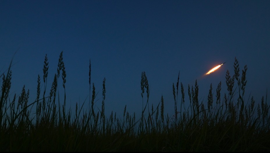 A rocket is fired above fields of wheat at night