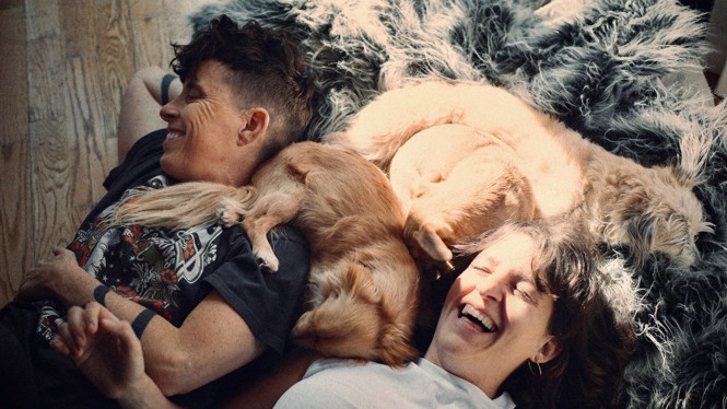 A guy and a girl laugh laying on the ground with dogs laying with them