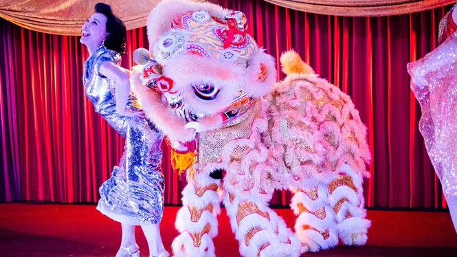 A woman dances on a stage with a dragon in front of a red curtain