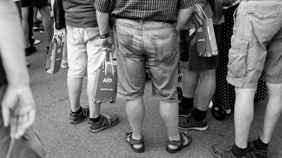 People stand in a crowd holding bags 