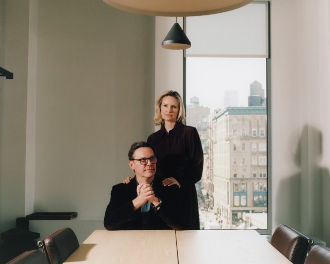 James and Kathryn in New York, with James seated hands folded at a conference table and Kathryn standing behind him, her hands on his shoulders