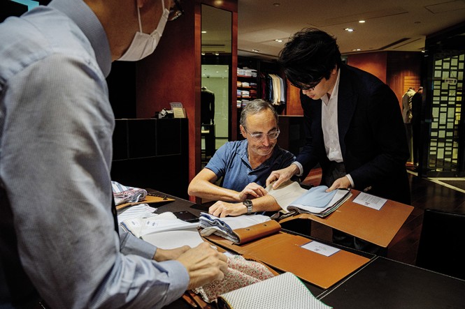 photo of Gary sitting and looking through fabric swatch books as two men look on