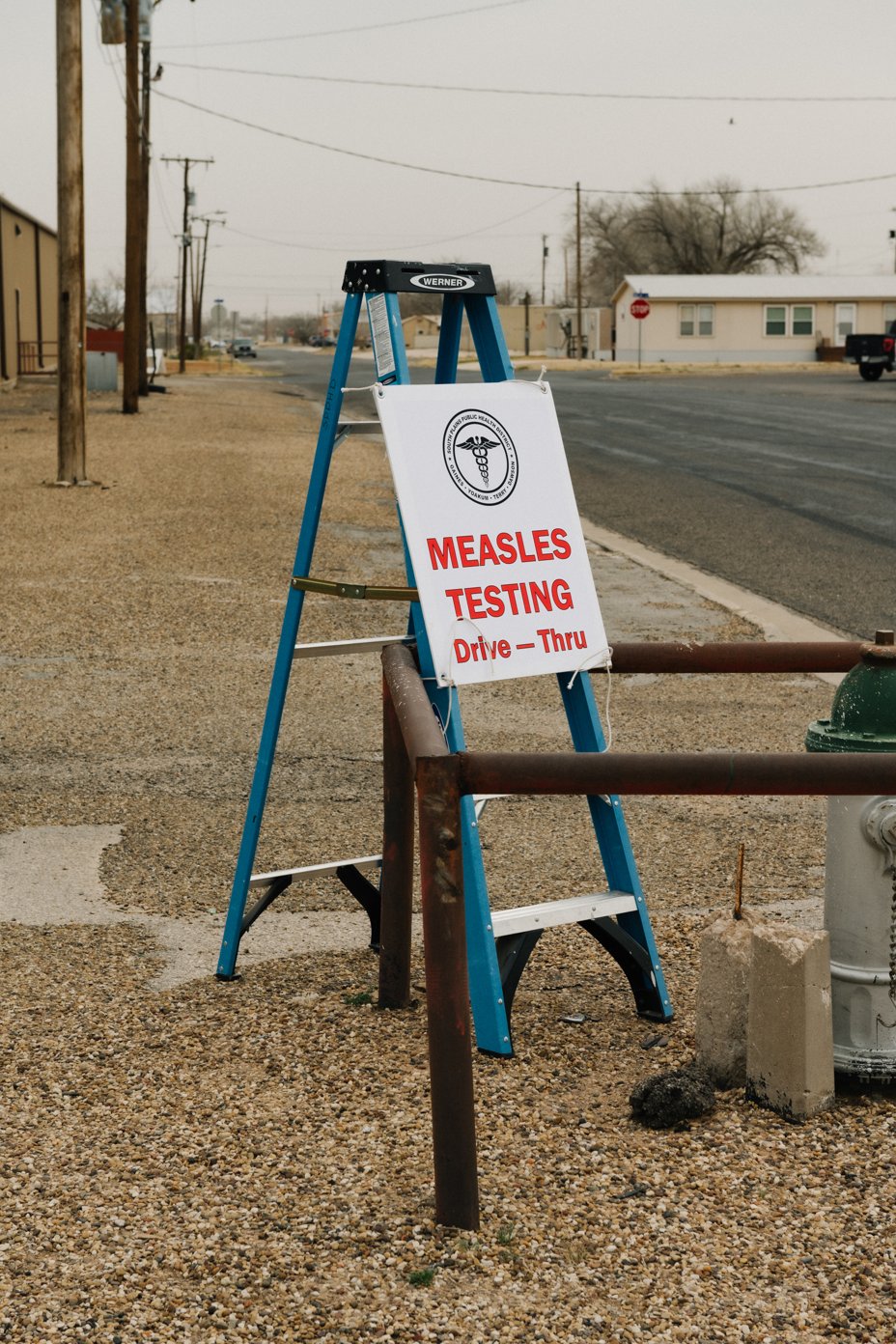 A sign with Measles Testing on it is tied up to a ladder