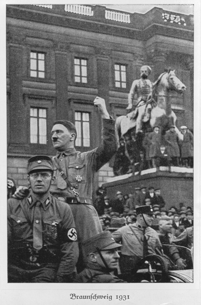 A photo of Hitler raising a fist in front of a statue.