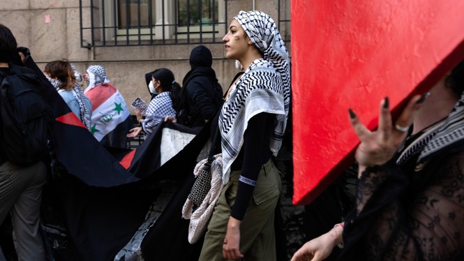 A woman wearing a Keffiyeh stands in a crowd during a protest