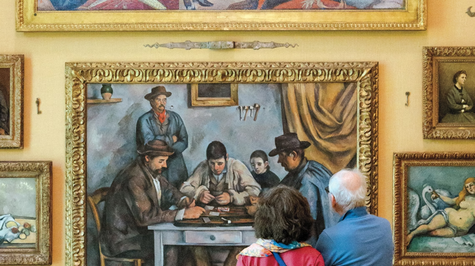 photo of the backs of two people looking at a wall of symmetrically arranged paintings including Seurat's 