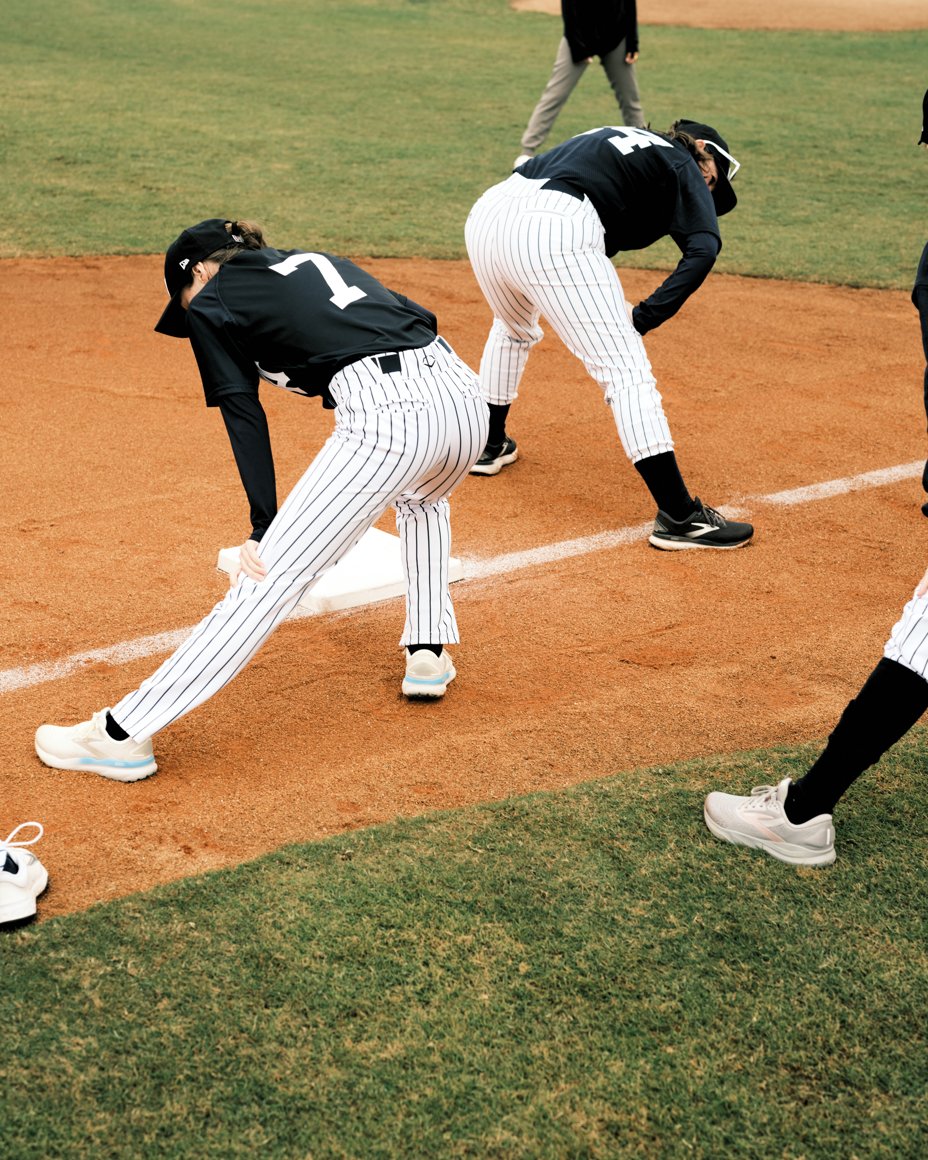 photo of women in baseball uniforms stretching on field 