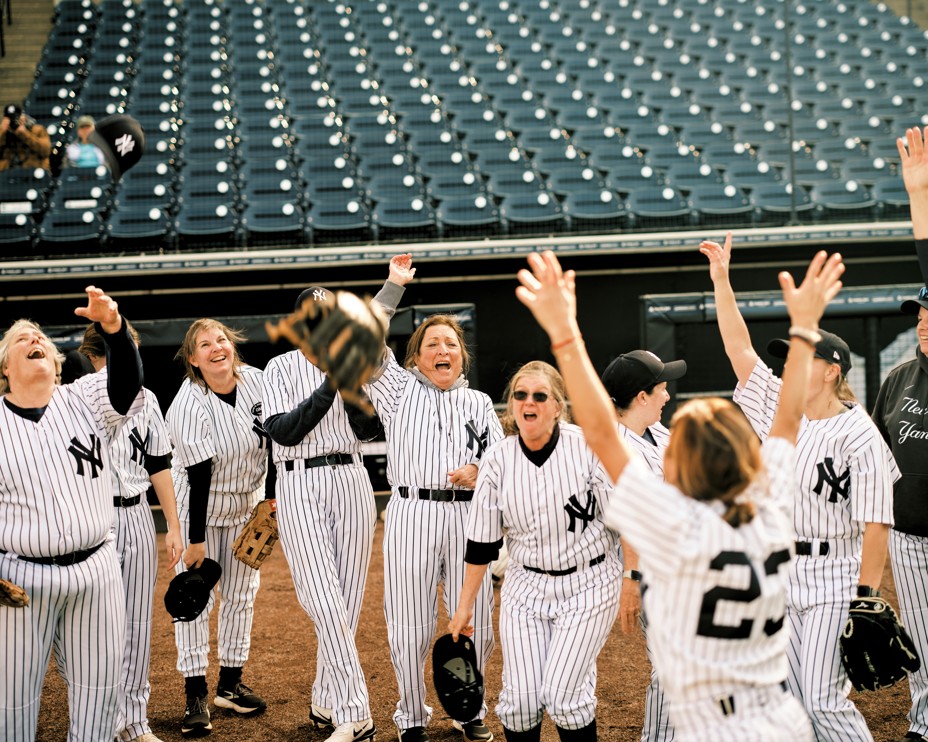 photo of group of women in baseball uniforms cheering and throwing hats in the air in celebration 