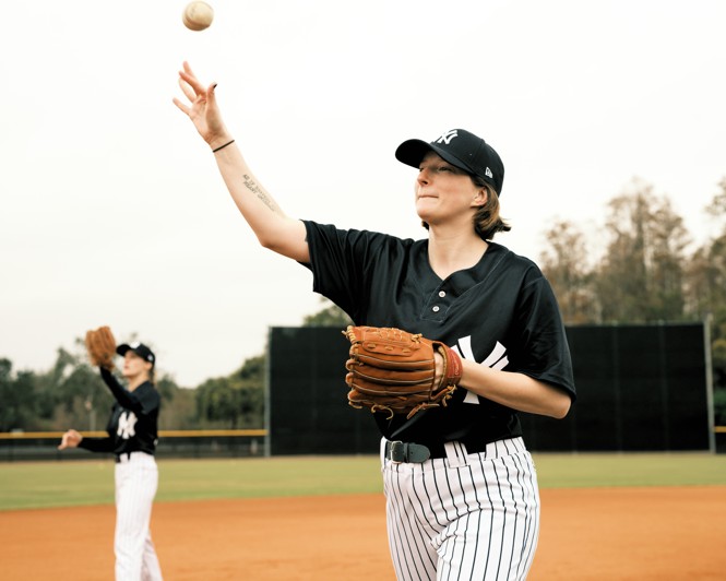 photo of woman in baseball uniform and glove throwing a ball