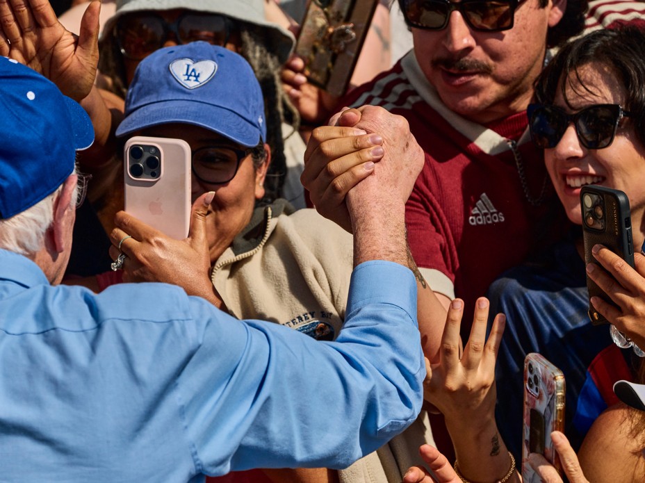 Bernie Sanders holds hands with a person in a crowd while others take photos of him