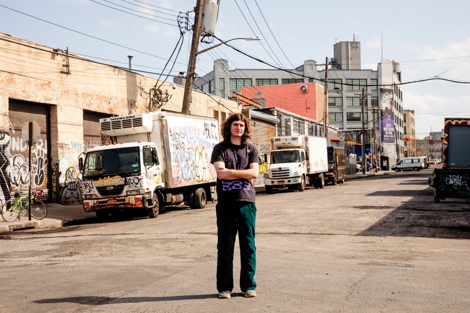 photo of person standing in street with industrial buildings and trucks covered with graffiti behind