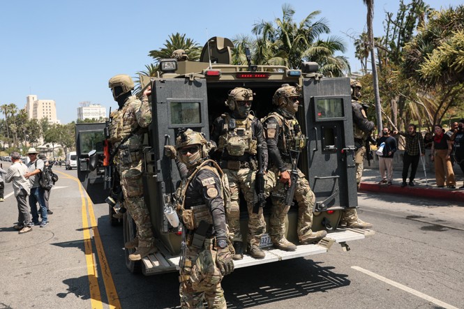 Federal agents with US Customs and Border Patrol (CBP) ride on an armored vehicle driving slowly down Wilshire Boulevard near MacArthur Park.