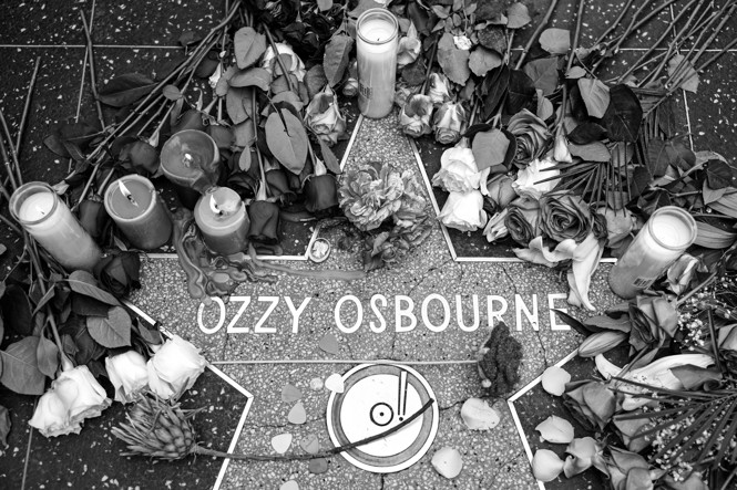 In a black a white photo, flowers and candles are displayed around Ozzy Osbourne's Hollywood star