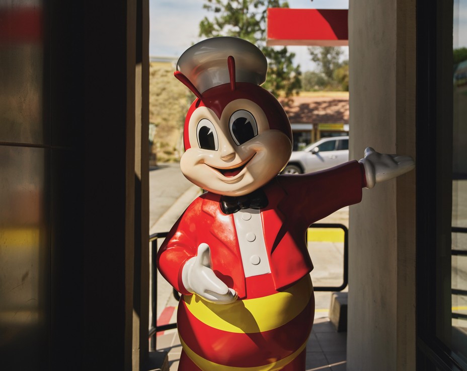 photo of lifesize bee statue in red jacket and white hat with arm outstretched inside fast-food restaurant