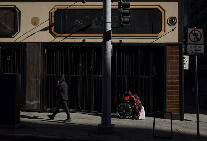 A person in a wheelchair is seen in the shadows on a street in San Francisco while anoter person walks by