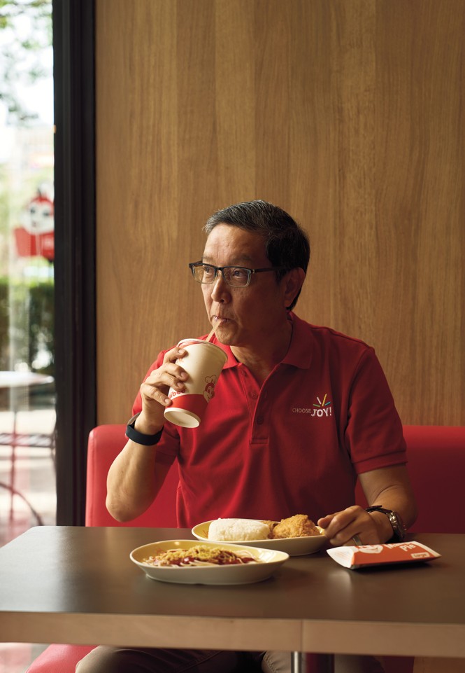 photo of man in glasses and red polo shirt sipping on a straw while seated at fast-food booth with meal before him