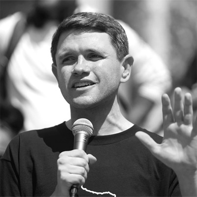 black-and-white photo of man speaking into mic with other hand raised
