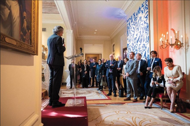 фото интерьера посольства с человеком, произносящим речь на слегка приподнятой платформе, и небольшой группой гостей, собравшихся вокруг и наблюдающих