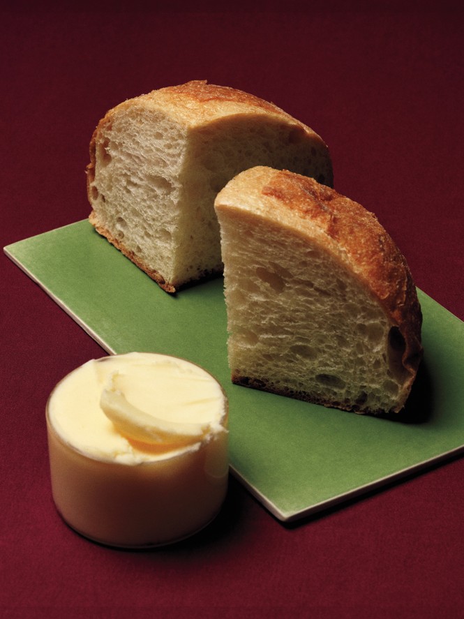 photo of 2 sliced quarters of a round boule of bread on green rectangular platter with round butter ramekin